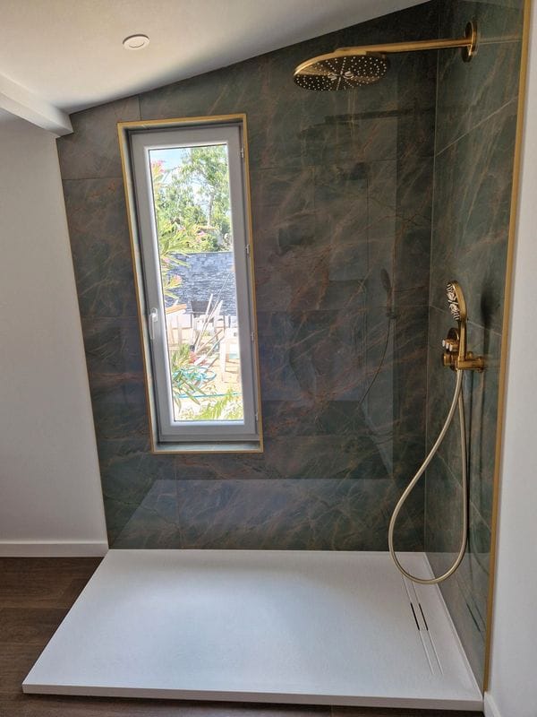 Douche contemporaine avec receveur blanc, carrelage mural effet pierre et robinetterie dorée design
