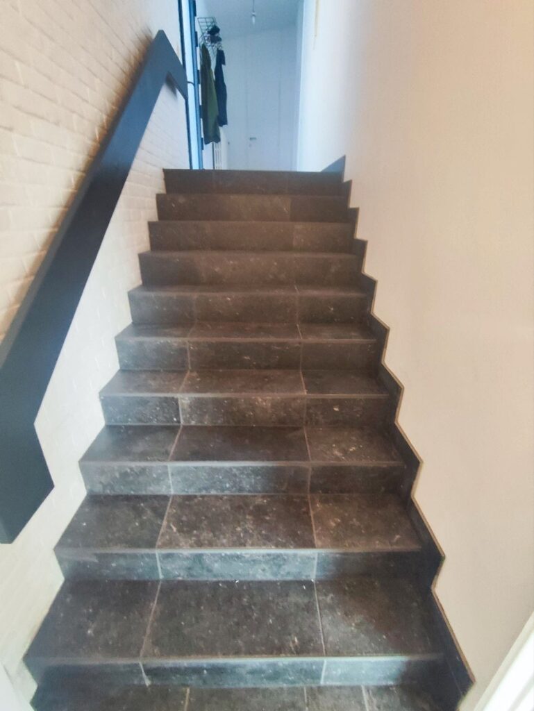 Escalier intérieur rénové avec marches en carrelage foncé et rampe noire sur mur blanc