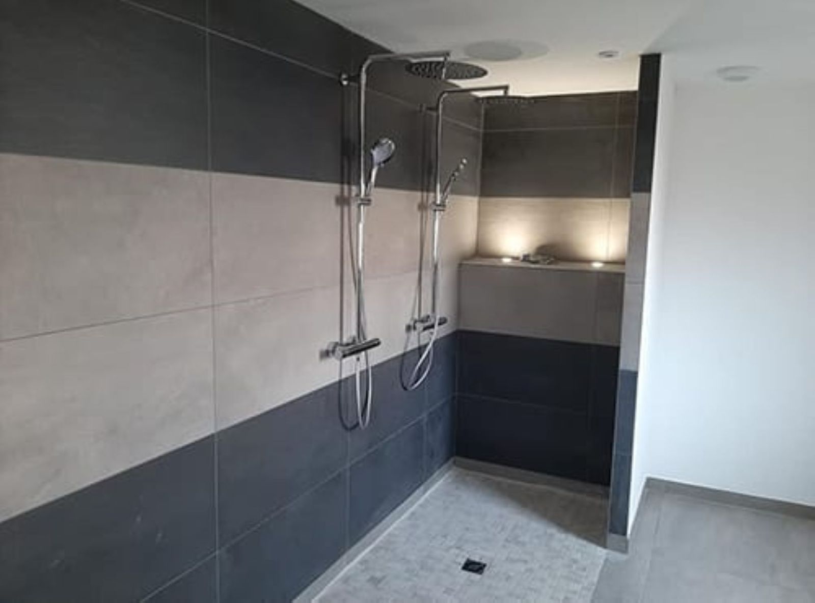 Salle de bain moderne avec douche à l’italienne, double pommeau de douche et carrelage mural bicolore gris